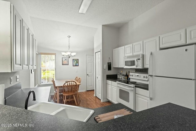 kitchen featuring a notable chandelier, dark countertops, white cabinetry, a sink, and white appliances