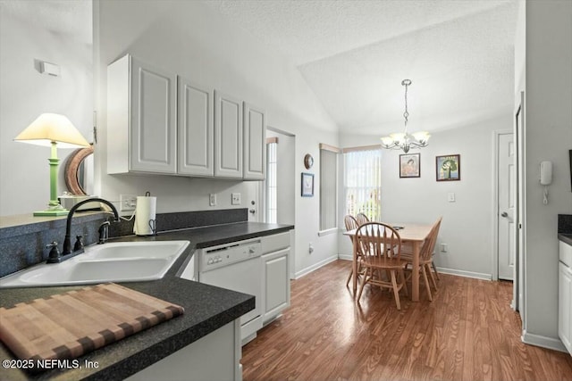 kitchen with dark countertops, dishwasher, lofted ceiling, and a sink