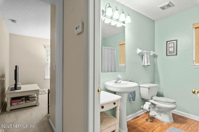 full bath featuring visible vents, toilet, a textured ceiling, wood finished floors, and baseboards