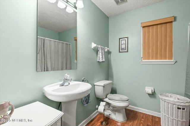 full bathroom with a textured ceiling, toilet, wood finished floors, baseboards, and a shower with curtain