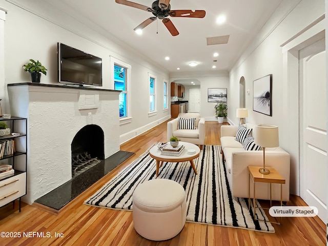 living room featuring visible vents, arched walkways, a fireplace with raised hearth, ceiling fan, and wood finished floors