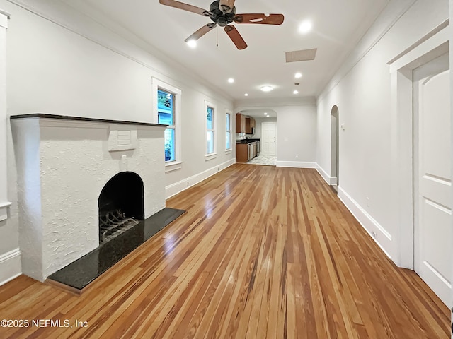 unfurnished living room featuring arched walkways, visible vents, a fireplace with raised hearth, light wood-style flooring, and baseboards