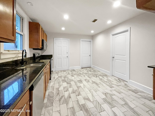 kitchen with visible vents, dark stone counters, brown cabinets, stainless steel appliances, and a sink