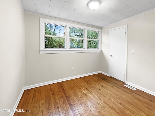 unfurnished room featuring visible vents, wood finished floors, a wealth of natural light, and baseboards