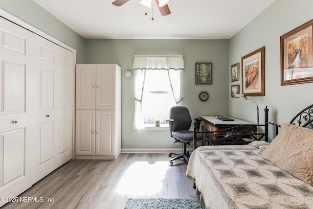 bedroom featuring light wood-style flooring, a textured ceiling, baseboards, and a ceiling fan