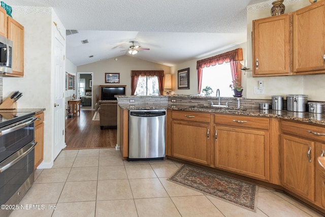 kitchen featuring light tile patterned floors, appliances with stainless steel finishes, open floor plan, a sink, and dark stone counters