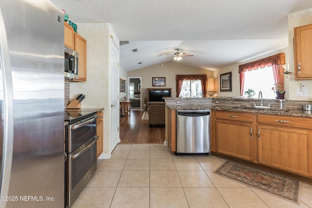 kitchen with lofted ceiling, appliances with stainless steel finishes, open floor plan, a sink, and light tile patterned flooring