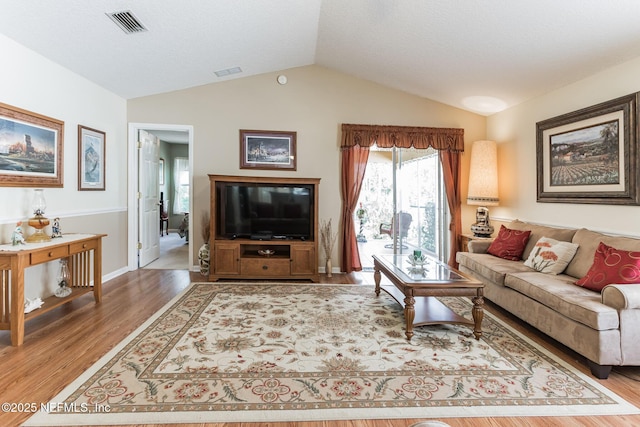 living room featuring vaulted ceiling, wood finished floors, and visible vents