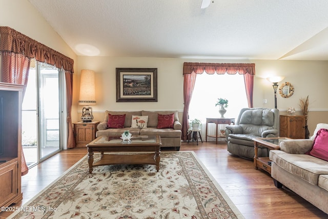 living area with a wealth of natural light, vaulted ceiling, a textured ceiling, and wood finished floors