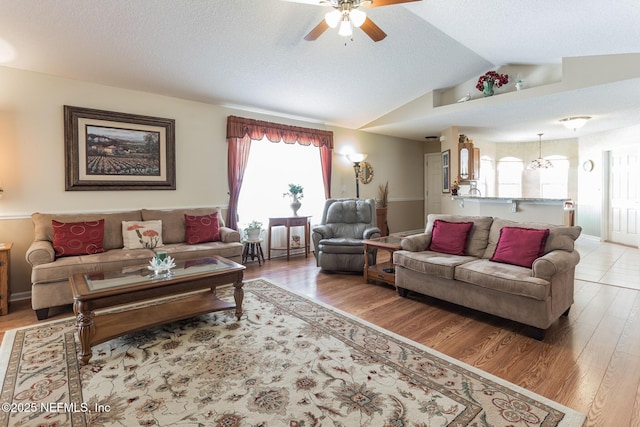 living area with a ceiling fan, vaulted ceiling, a textured ceiling, and wood finished floors