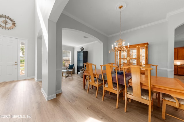 dining room featuring arched walkways, a notable chandelier, light wood-style flooring, ornamental molding, and baseboards