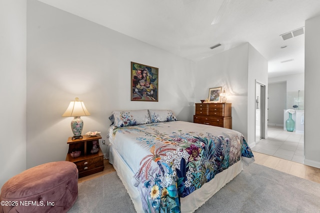 bedroom featuring wood finished floors, ensuite bath, visible vents, and baseboards