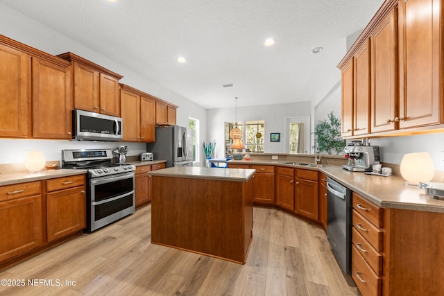 kitchen featuring a textured ceiling, light wood-style flooring, stainless steel appliances, a sink, and brown cabinets