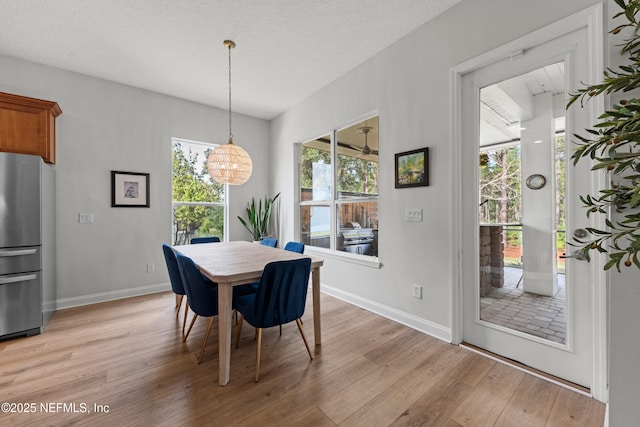 dining space featuring a textured ceiling, light wood-style flooring, and baseboards