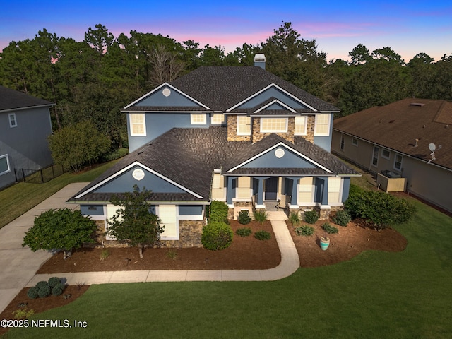 traditional-style home featuring a porch, a front yard, stone siding, and fence