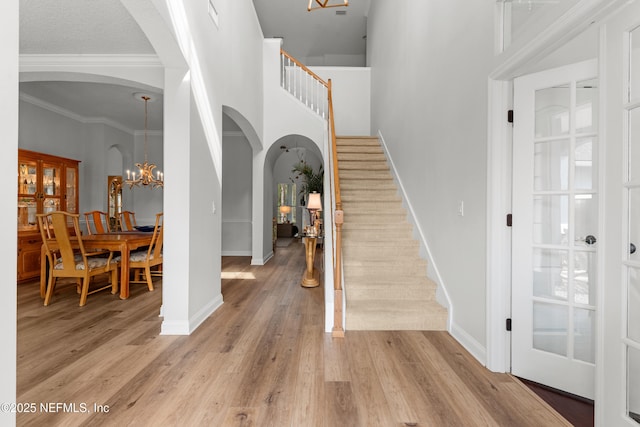 foyer entrance featuring light wood-style floors, arched walkways, baseboards, and stairs