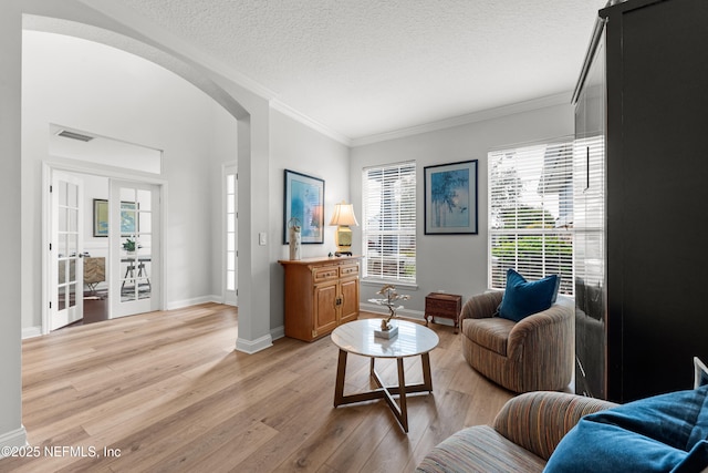 living area featuring arched walkways, light wood finished floors, ornamental molding, a textured ceiling, and baseboards