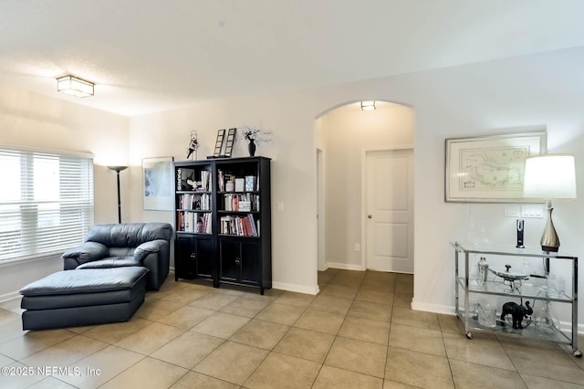 living area featuring light tile patterned floors, baseboards, and arched walkways