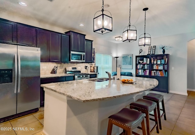 kitchen with light stone countertops, a kitchen island with sink, stainless steel appliances, pendant lighting, and backsplash