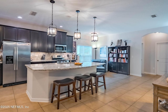 kitchen featuring appliances with stainless steel finishes, pendant lighting, a kitchen island with sink, and visible vents