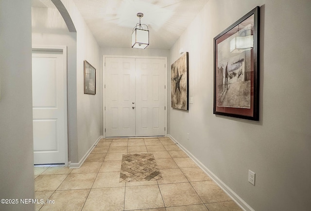 hall with light tile patterned flooring, arched walkways, and baseboards