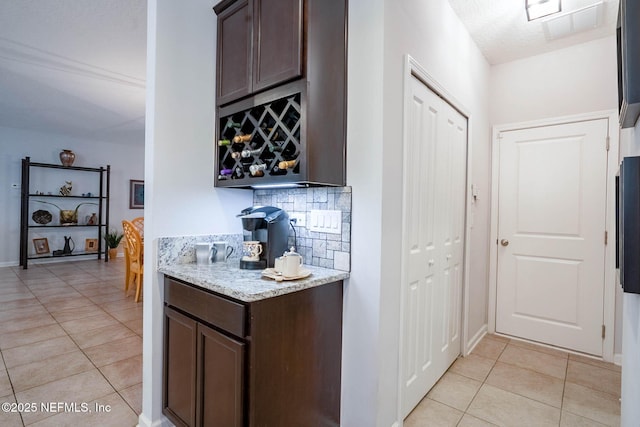 kitchen featuring light tile patterned flooring, dark brown cabinetry, backsplash, and light stone countertops