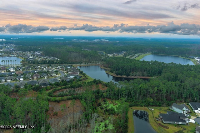 aerial view at dusk featuring a wooded view and a water view