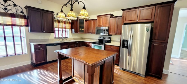 kitchen with dark wood-type flooring, pendant lighting, a sink, appliances with stainless steel finishes, and baseboards