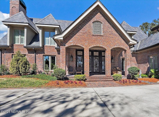 view of front of home with a high end roof, a chimney, and brick siding