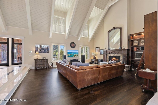 living room featuring dark wood finished floors, high vaulted ceiling, a warm lit fireplace, beamed ceiling, and baseboards