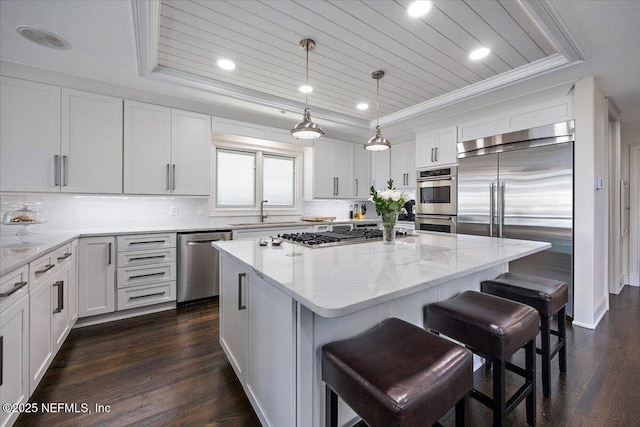 kitchen featuring light stone counters, a kitchen island, white cabinets, appliances with stainless steel finishes, and a tray ceiling