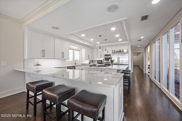 kitchen featuring visible vents, hanging light fixtures, appliances with stainless steel finishes, white cabinets, and a peninsula