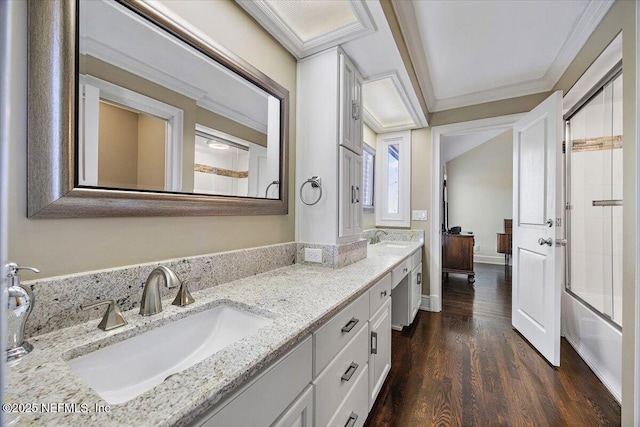 bathroom featuring double vanity, bath / shower combo with glass door, ornamental molding, a sink, and wood finished floors