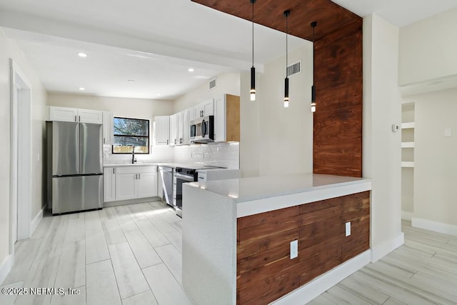 kitchen with stainless steel appliances, light countertops, white cabinetry, and decorative light fixtures