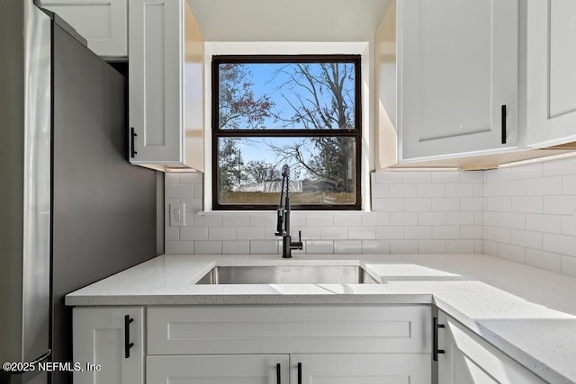 kitchen featuring light stone counters, a sink, white cabinetry, freestanding refrigerator, and tasteful backsplash