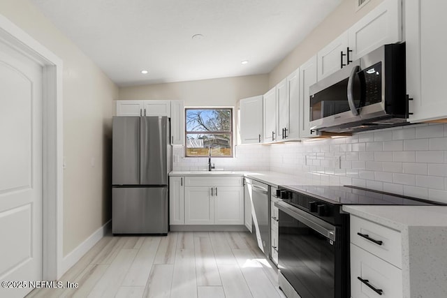 kitchen with white cabinets, tasteful backsplash, stainless steel appliances, and light countertops