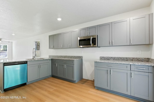 kitchen featuring stainless steel microwave, a sink, ceiling fan, light wood-type flooring, and dishwashing machine