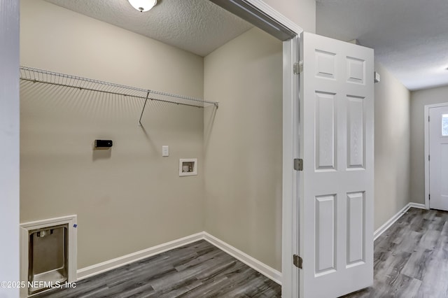 clothes washing area with hookup for a washing machine, a textured ceiling, baseboards, and wood finished floors