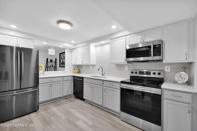 kitchen with appliances with stainless steel finishes, light countertops, light wood-type flooring, white cabinetry, and a sink