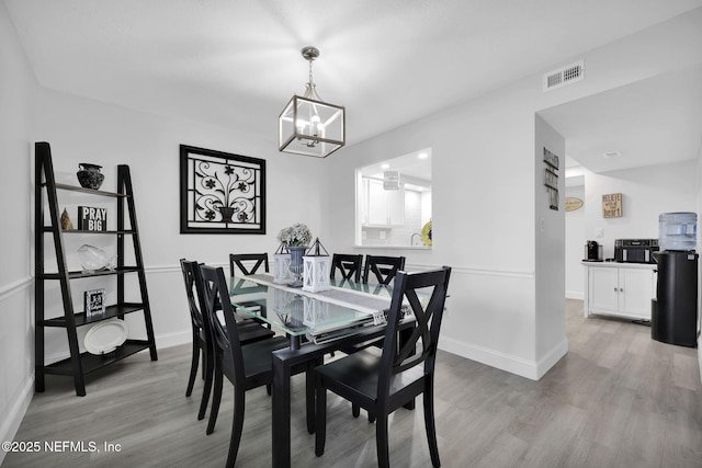 dining room with light wood-type flooring, an inviting chandelier, baseboards, and visible vents