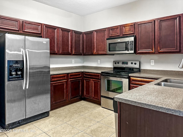 kitchen featuring a textured ceiling, light tile patterned floors, a sink, appliances with stainless steel finishes, and reddish brown cabinets