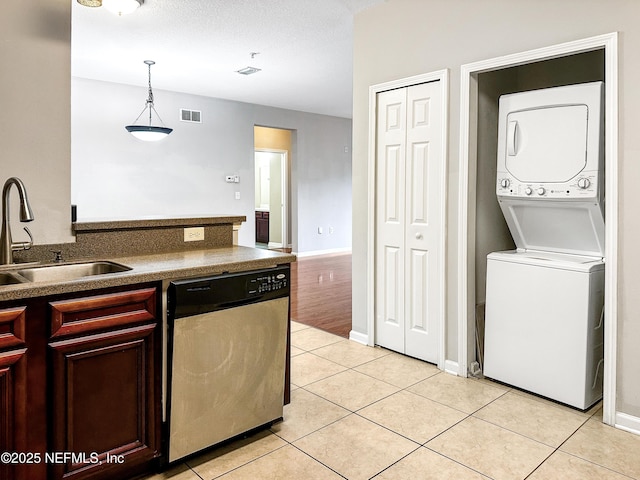 kitchen featuring stacked washer / drying machine, stainless steel dishwasher, pendant lighting, a sink, and light tile patterned flooring