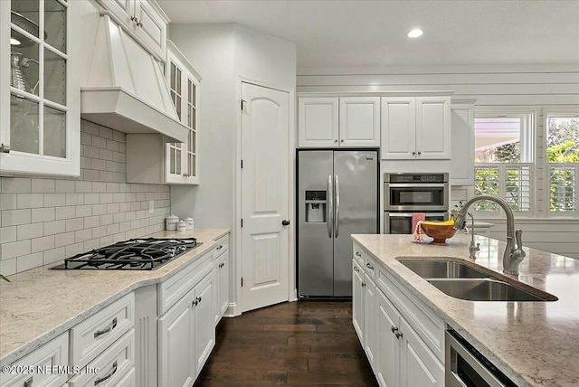 kitchen with appliances with stainless steel finishes, dark wood-style flooring, custom exhaust hood, white cabinetry, and a sink