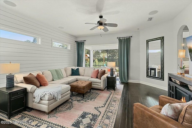 living room featuring arched walkways, a ceiling fan, visible vents, baseboards, and hardwood / wood-style floors