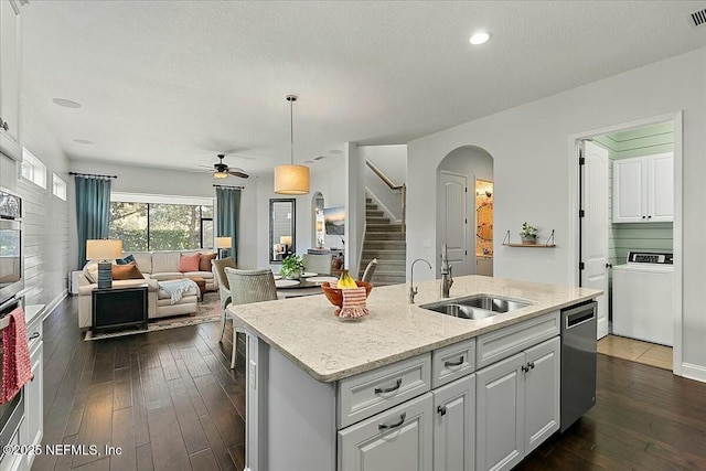 kitchen with dark wood-style floors, arched walkways, stainless steel appliances, washer / clothes dryer, and a sink