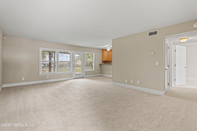 unfurnished living room with light colored carpet, visible vents, a ceiling fan, a textured ceiling, and baseboards