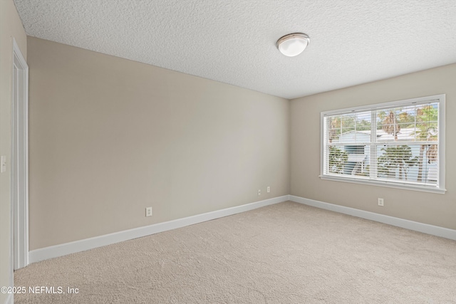 empty room with light carpet, baseboards, and a textured ceiling