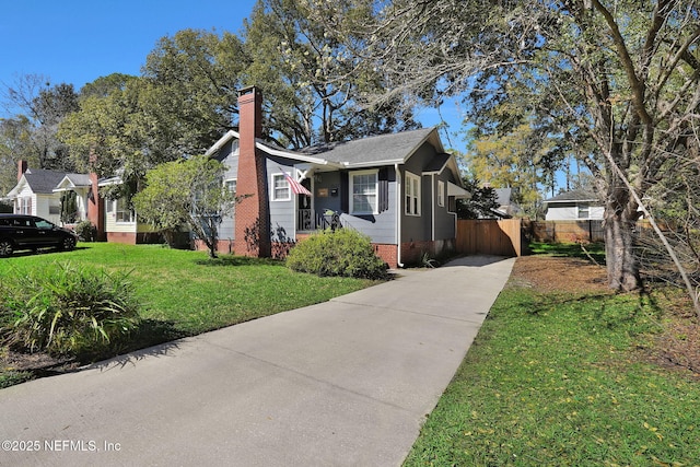 bungalow featuring driveway, a chimney, fence, and a front yard