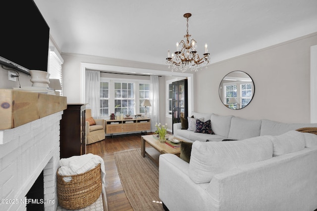 living area with ornamental molding, a fireplace, an inviting chandelier, and wood finished floors