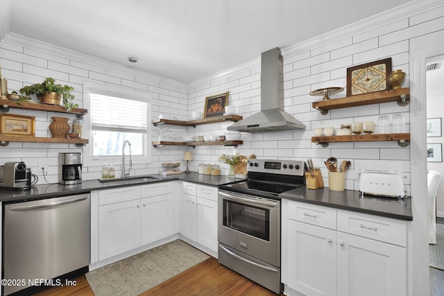 kitchen featuring open shelves, dark countertops, appliances with stainless steel finishes, a sink, and wall chimney range hood